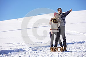 Young playful couple having fun sledging down snow covered hill