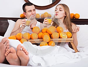 Young pleasant couple with ripe oranges and freshly juice