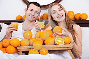 Young pleasant smiling couple with ripe oranges and freshly juice