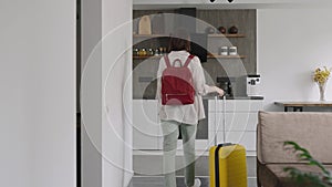 A young pleasant woman moves into a rented apartment. The tourist arrived with a yellow suitcase and backpack.