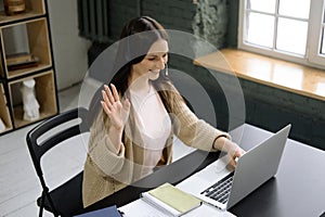 Young cheerful cute beautiful business woman sit indoors in office using laptop computer with headset.