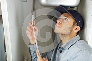 Young plumber fitting flexible pipe under kitchen sink