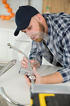 young plumber installing tap in kitchen