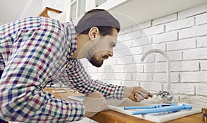 Young plumber or repairman is fixing or installing a mixer faucet in the kitchen