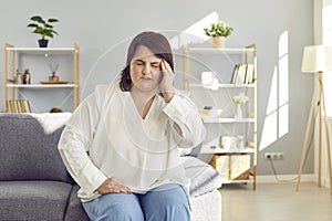 Young plump overweight woman sitting on the couch suffering from headache.