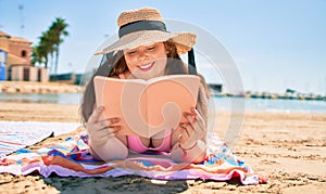 Young plus size overweight woman reading a book relaxing at the beach on summer holidays
