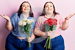 Young plus size twins holding flowers celebrating victory with happy smile and winner expression with raised hands