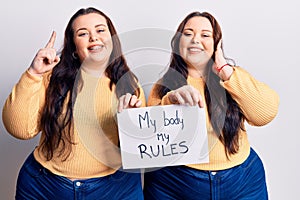 Young plus size twins holding my body my rules banner surprised with an idea or question pointing finger with happy face, number