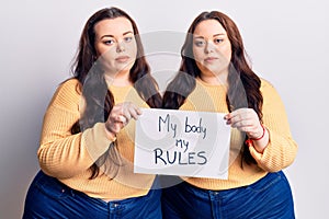 Young plus size twins holding my body my rules banner thinking attitude and sober expression looking self confident