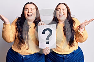 Young plus size twins holding question mark celebrating victory with happy smile and winner expression with raised hands