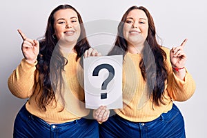 Young plus size twins holding question mark smiling happy pointing with hand and finger to the side