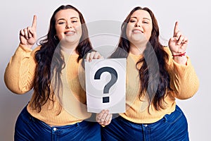 Young plus size twins holding question mark surprised with an idea or question pointing finger with happy face, number one