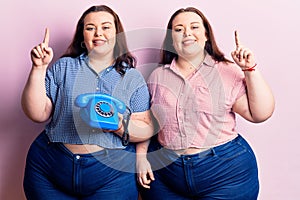 Young plus size twins holding vintage telephone surprised with an idea or question pointing finger with happy face, number one