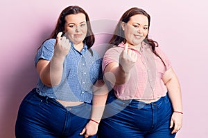 Young plus size twins wearing casual clothes beckoning come here gesture with hand inviting welcoming happy and smiling