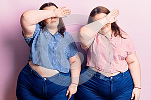 Young plus size twins wearing casual clothes covering eyes with arm, looking serious and sad