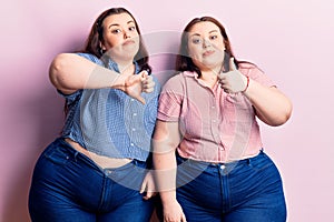 Young plus size twins wearing casual clothes doing thumbs up and down, disagreement and agreement expression