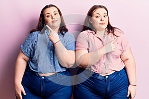 Young plus size twins wearing casual clothes pointing to both sides with fingers, different direction disagree