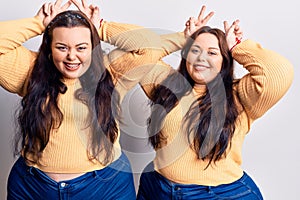 Young plus size twins wearing casual clothes posing funny and crazy with fingers on head as bunny ears, smiling cheerful