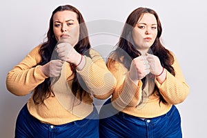 Young plus size twins wearing casual clothes ready to fight with fist defense gesture, angry and upset face, afraid of problem