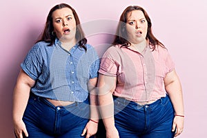 Young plus size twins wearing casual clothes in shock face, looking skeptical and sarcastic, surprised with open mouth
