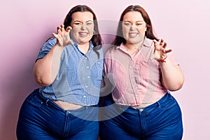 Young plus size twins wearing casual clothes smiling funny doing claw gesture as cat, aggressive and sexy expression