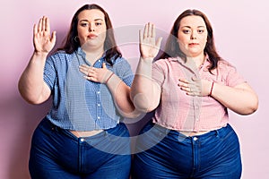 Young plus size twins wearing casual clothes swearing with hand on chest and open palm, making a loyalty promise oath