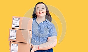 Young plus size woman holding delivery package looking positive and happy standing and smiling with a confident smile showing