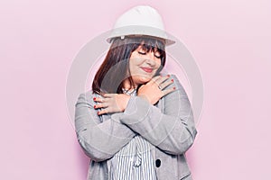 Young plus size woman wearing architect hardhat hugging oneself happy and positive, smiling confident