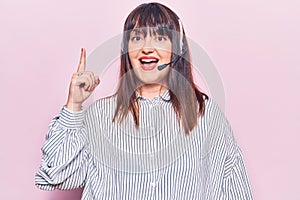 Young plus size woman wearing call center agent headset pointing finger up with successful idea