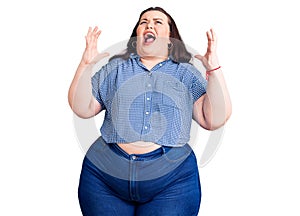 Young plus size woman wearing casual clothes crazy and mad shouting and yelling with aggressive expression and arms raised