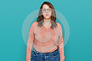Young plus size woman wearing casual clothes and glasses puffing cheeks with funny face