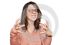 Young plus size woman wearing casual clothes and glasses shouting frustrated with rage, hands trying to strangle, yelling mad