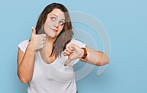 Young plus size woman wearing casual white t shirt doing thumbs up and down, disagreement and agreement expression