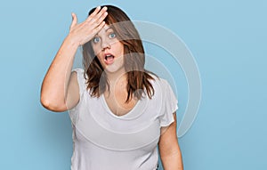 Young plus size woman wearing casual white t shirt surprised with hand on head for mistake, remember error