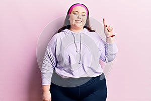 Young plus size woman wearing sportswear smiling with an idea or question pointing finger up with happy face, number one