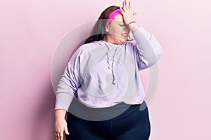 Young plus size woman wearing sportswear surprised with hand on head for mistake, remember error