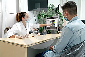 A young podiatrist wearing a mask explains the diagnosis to a young patient in her office