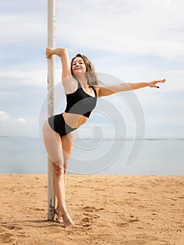 Young pole dance woman posing on the beach. Fit slim body. Attractive Caucasian woman wearing black sportswear. Fitness, wellness