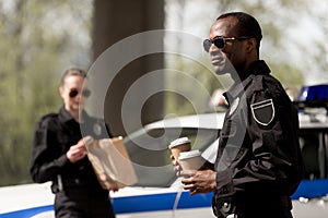 young police officers with coffee to go and paper bag with lunch