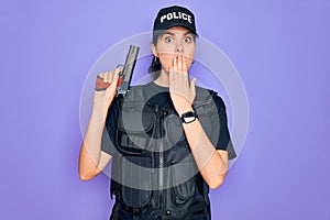 Young police woman wearing security bulletproof vest uniform and holding gun cover mouth with hand shocked with shame for mistake,