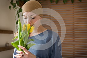 Young positive adult female cancer patient holding bouquet of yellow tulips and smiling. Fighting with cancer.