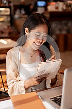 A young positive Asian female college student studying online and doing homework at a coffee shop