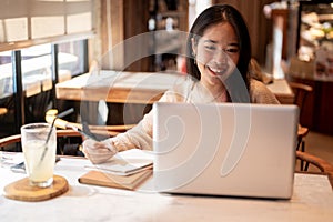 A young positive Asian female college student studying online and doing homework at a coffee shop