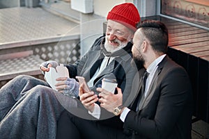 Young positive businessman and mature beggar look at phone