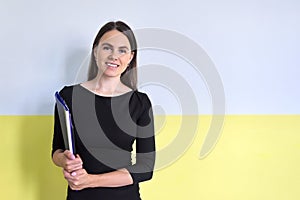 Young positive businesswoman with folder in hand smiling looking at camera