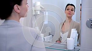 Young positive businesswoman in suit preening looking at mirror in bathroom.