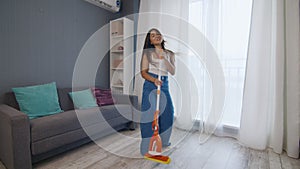 Young positive caucasian woman funnily dancing while cleaning the house