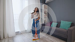 Young positive caucasian woman funnily dancing while cleaning the house
