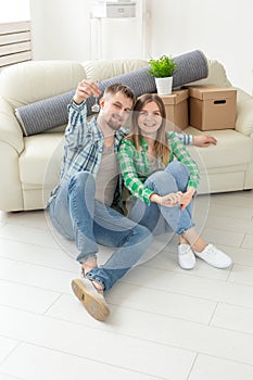 Young positive couple holding keys to a new apartment while standing in their living room. Housewarming and family