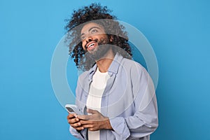 Young positive ethnic Arabian man holding mobile phone and smiling looking up